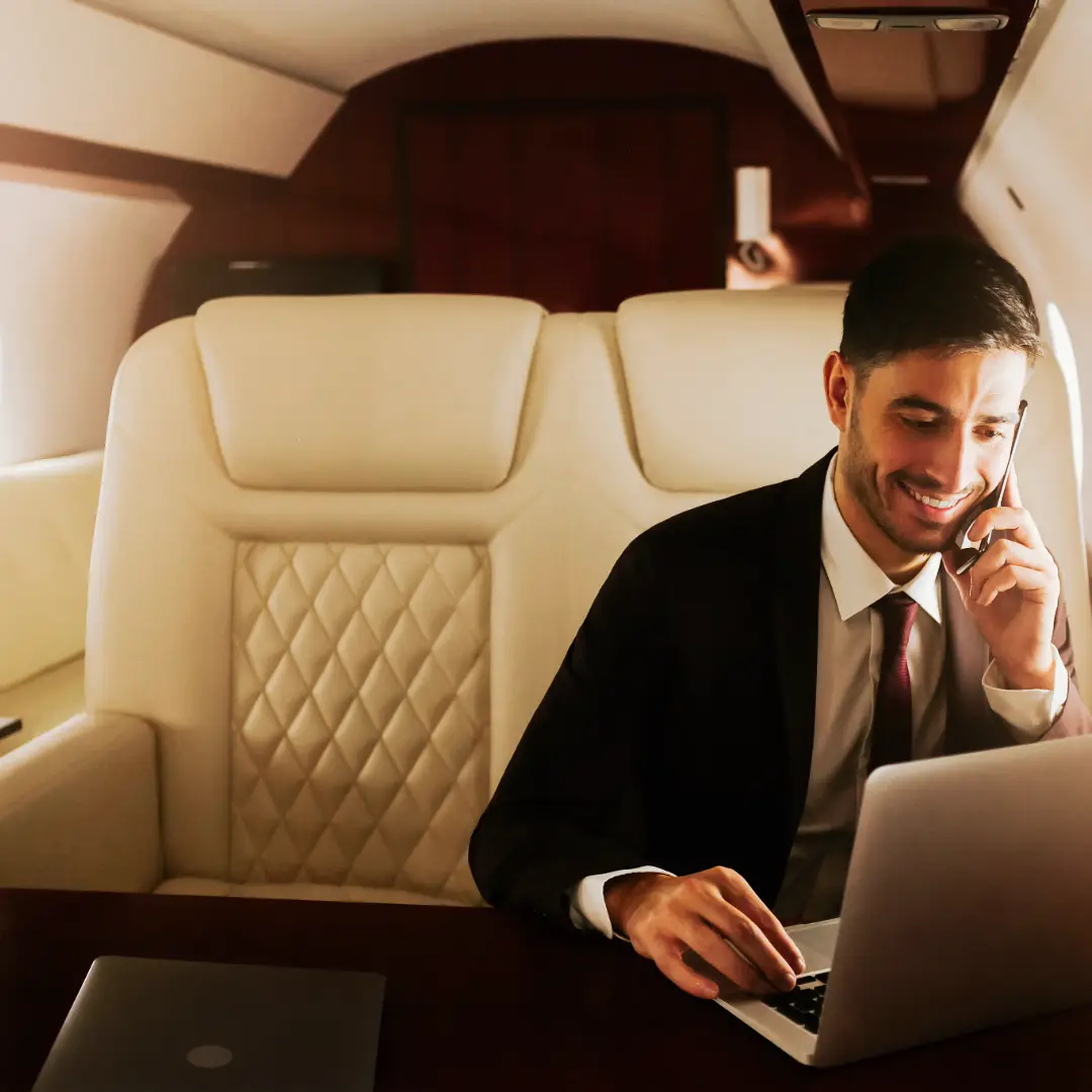 CEO or Executive manager during a private flight on luxurious leather seats with diamond stitches , talking on his phone and working using his laptop on dark wood table inferno of him - AERONOVA FLIGHT SUPPORT
